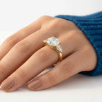 Three-stone radiant cut moissanite engagement ring with two pear-shaped side stones set in polished yellow gold, worn on a hand.