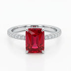 An emerald-cut red ruby ring with a silver-colored band paved with small diamonds, shown on a clean white background.