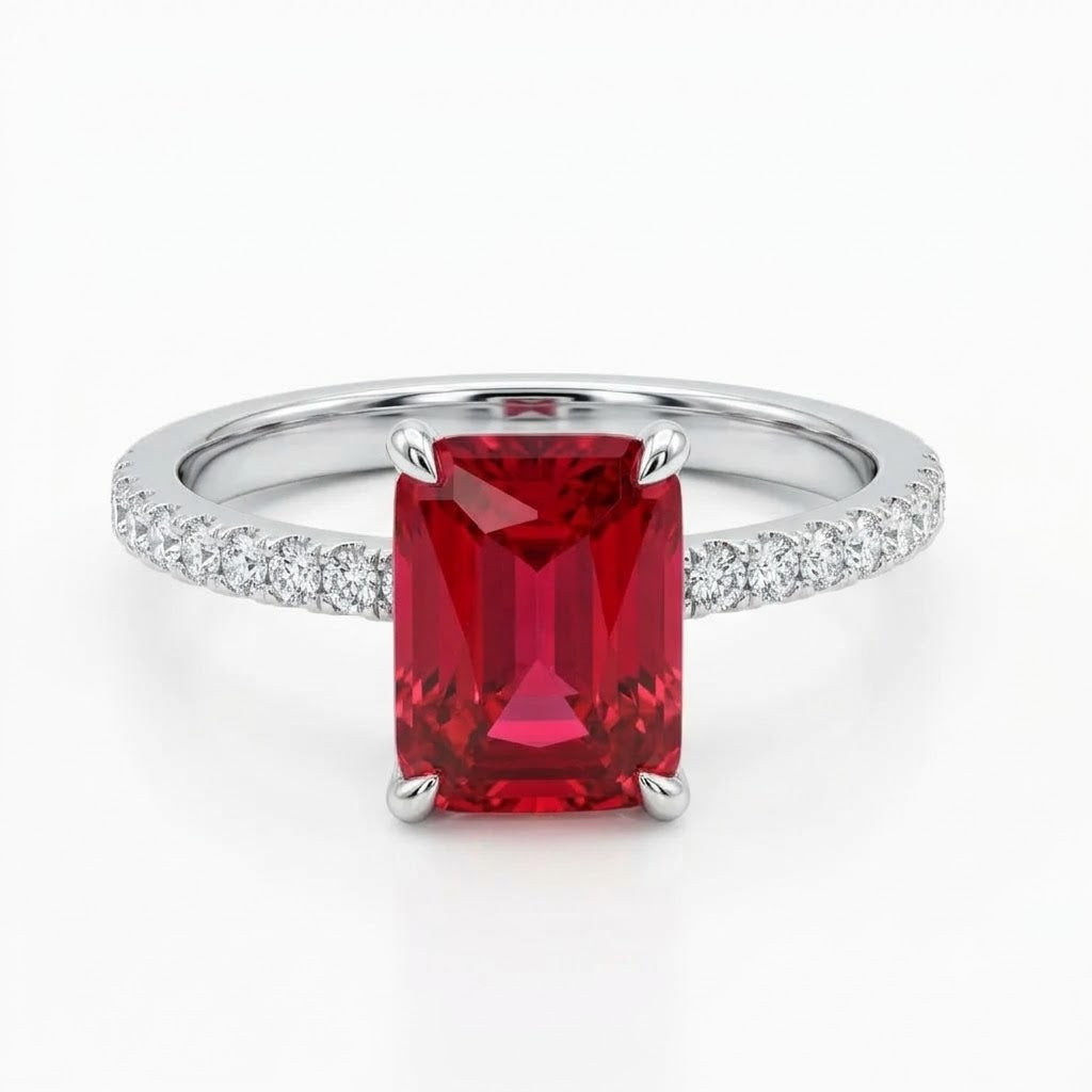 An emerald-cut red ruby ring with a silver-colored band paved with small diamonds, shown on a clean white background.