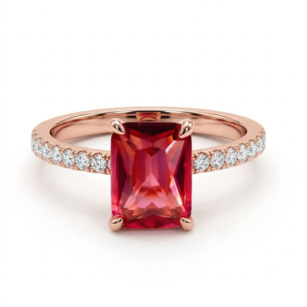 A rose gold ring featuring a large rectangular emerald-cut red gemstone in the center, with a pavé band set with small clear stones, shown on a white background.