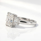 Side profile view of a three-stone radiant cut engagement ring in white gold or platinum, featuring cropped-corner trapezoid side stones and a four-prong basket setting.