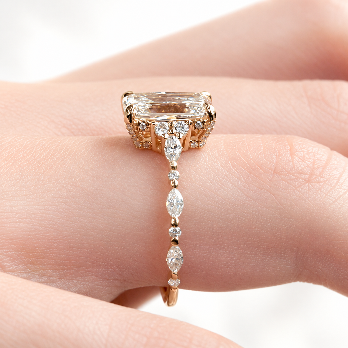Rose gold radiant cut ring side profile with diamond trio, hidden halo, and marquise band on finger
