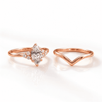 Rose gold bridal set showing a marquise diamond ring with side accent stones beside a matching V-shaped chevron band, displayed on a glossy white surface.