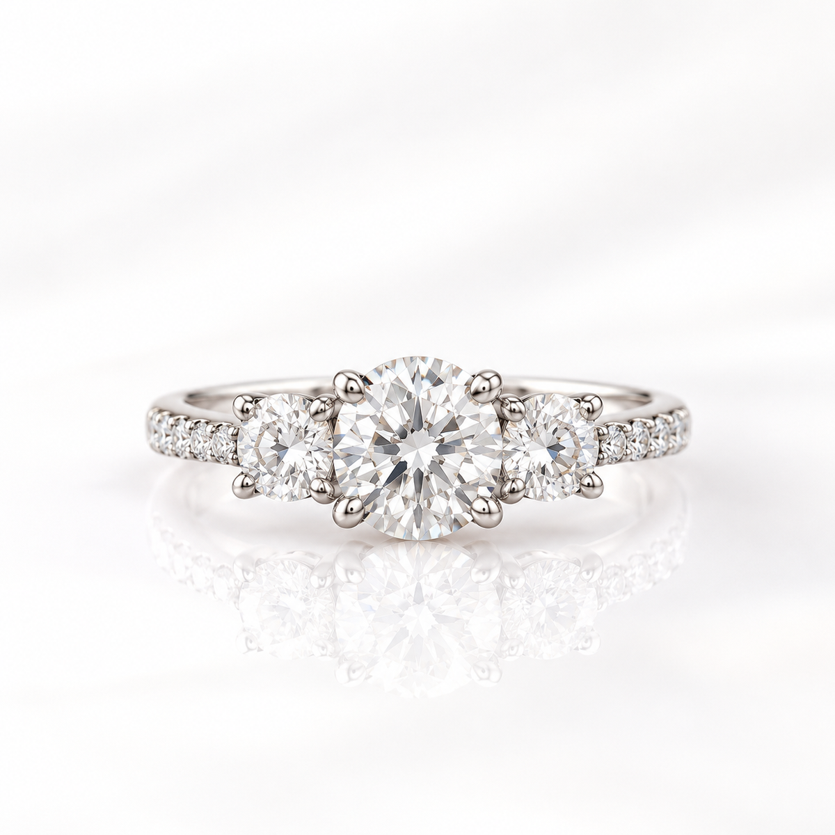 Round cut diamond center stone in a four-prong white gold setting, flanked by a round side stone on each side with a pavé diamond band