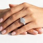Vintage-inspired round cut diamond engagement ring set in white gold, featuring a hexagonal halo with milgrain detailing and round bezel-set side accents, worn on a hand.