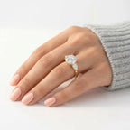 Round cut diamond engagement ring with two pear-shaped side stones set in yellow gold, worn on the ring finger.