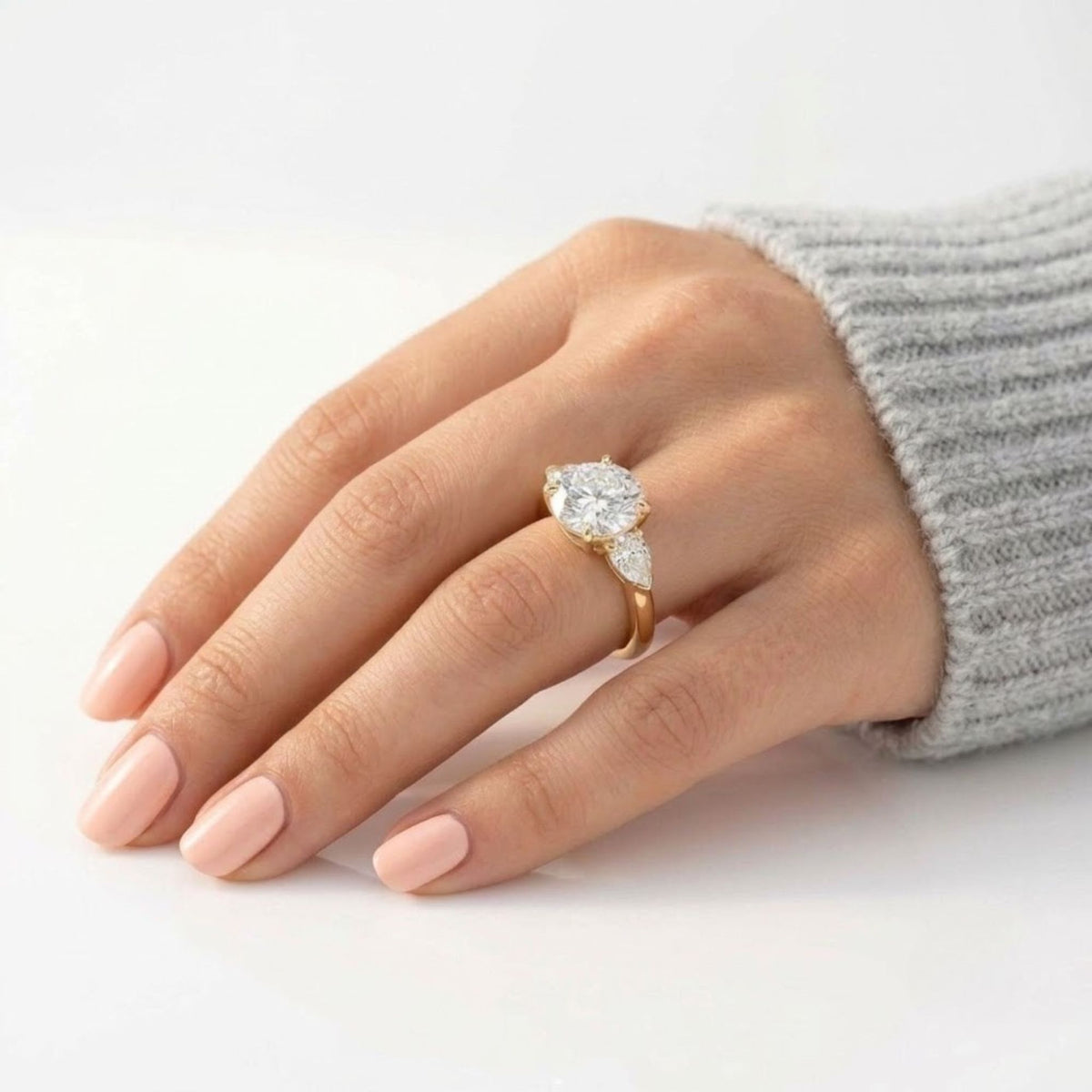 Round cut diamond engagement ring with two pear-shaped side stones set in yellow gold, worn on the ring finger.