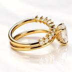 Side view of a yellow gold bypass ring showing the oval diamond's hidden halo of tiny pavé diamonds beneath the stone and the graduated round diamonds rising along the split shank.