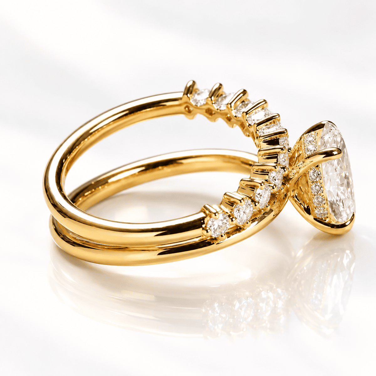 Side view of a yellow gold bypass ring showing the oval diamond's hidden halo of tiny pavé diamonds beneath the stone and the graduated round diamonds rising along the split shank.