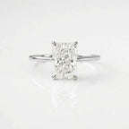 High-quality, ultra-realistic product photograph of a solitaire engagement ring featuring a large, radiant-cut center diamond held by four prongs. The ring has a simple, polished silver band. It is positioned in a balanced, lying position on a clean pure white background with soft studio lighting and subtle natural shadows. The reflection of the ring and diamond is visible on the surface.