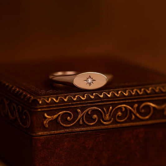A close-up view of a gold signet ring featuring a delicate engraved starburst design with a sparkling round diamond set in the center,
