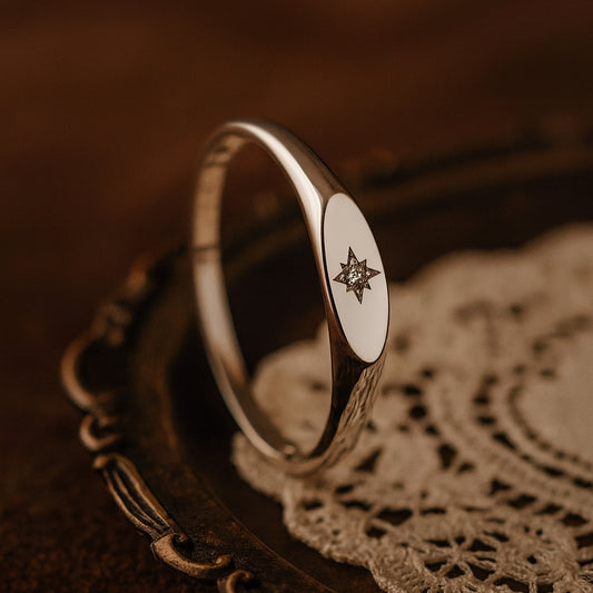 A close-up view of a gold signet ring featuring a delicate engraved starburst design with a sparkling round diamond set in the center,
