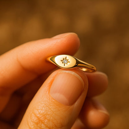 A close-up view of a gold signet ring featuring a delicate engraved starburst design with a sparkling round diamond set in the center,
