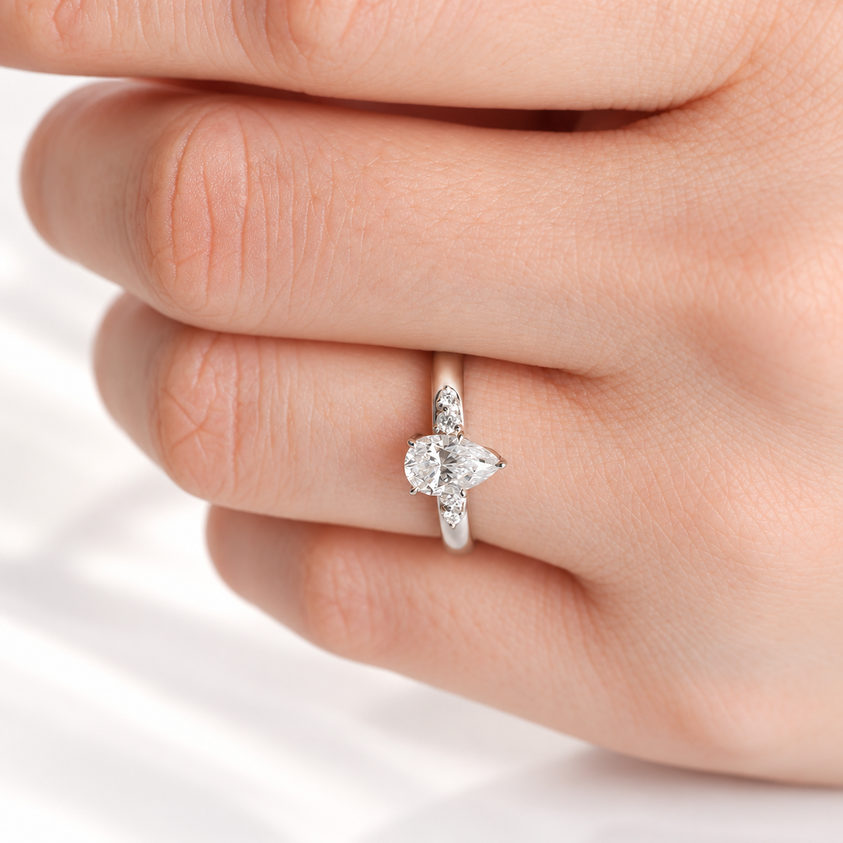 Teardrop engagement ring with a pear cut diamond center stone in a prong white gold setting and round side stones on each side of the band