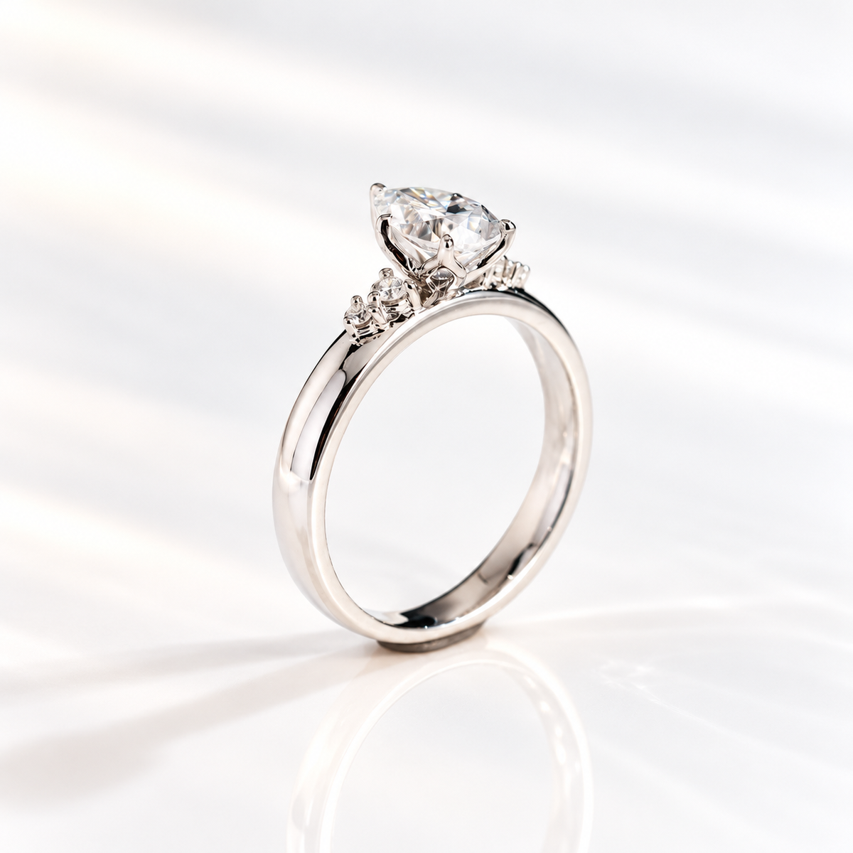 Three-quarter view of a teardrop engagement ring with a pear cut diamond center stone in a five-prong white gold setting and round side stones on a thick band