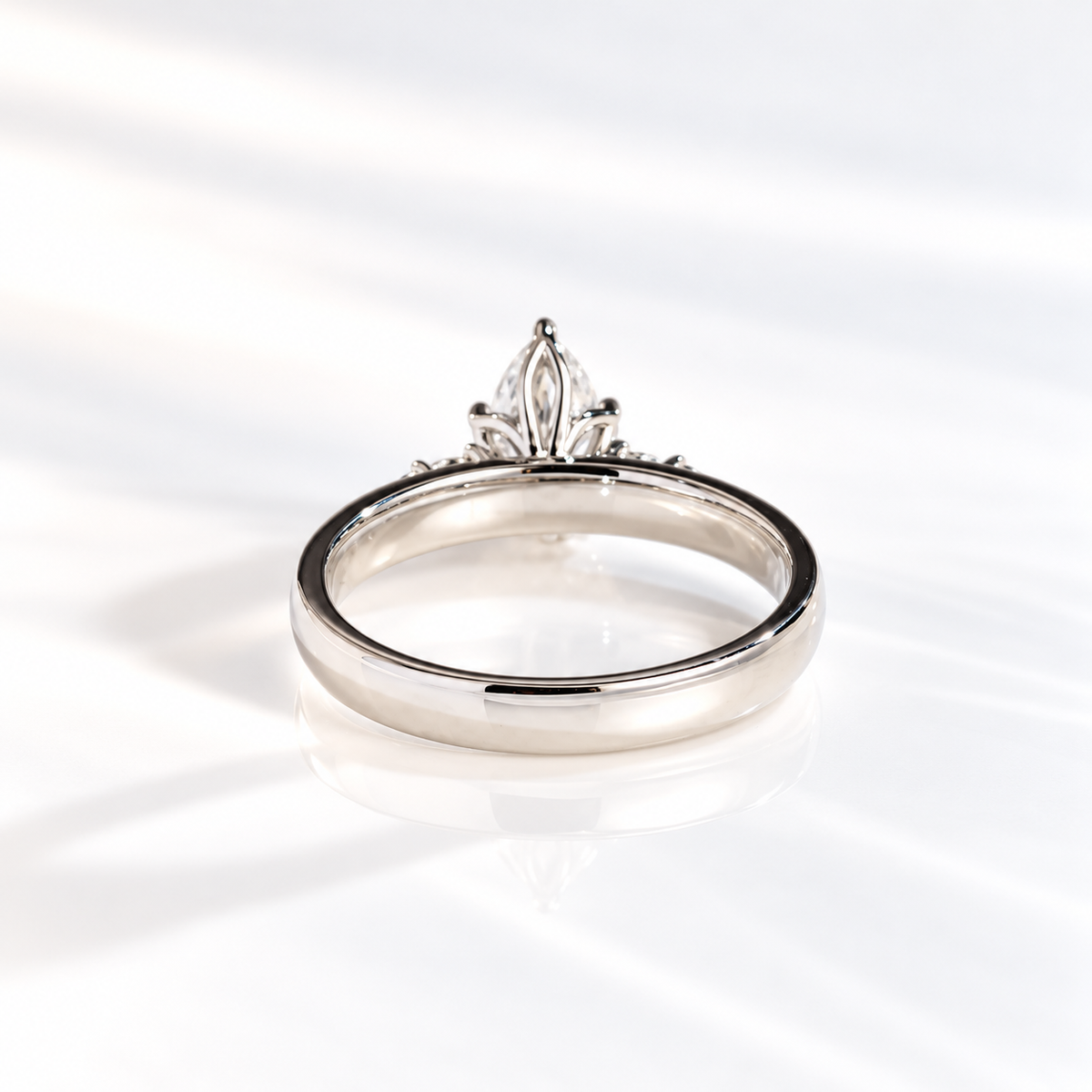 Back view of a teardrop solitaire engagement ring showing the prong setting of a pear cut diamond and the thick polished white gold band