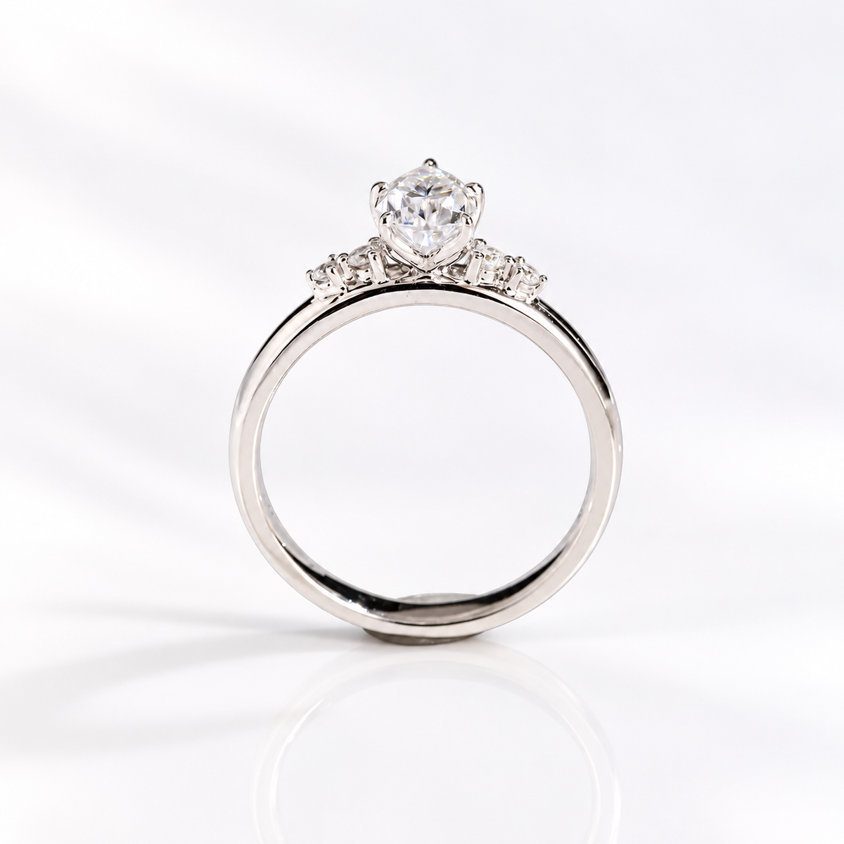 Side profile of a teardrop solitaire engagement ring with a pear cut diamond in a five-prong white gold setting and round side stones along the shoulders of a thick band