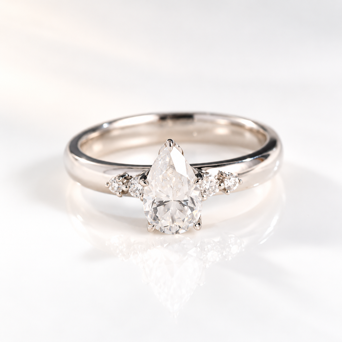 Teardrop solitaire engagement ring with a pear cut diamond center stone in a five-prong white gold setting, with two round side stones on each side of a thick band
