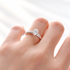 Teardrop solitaire engagement ring with a pear cut diamond center stone in a five-prong white gold setting, with round side stones on each side