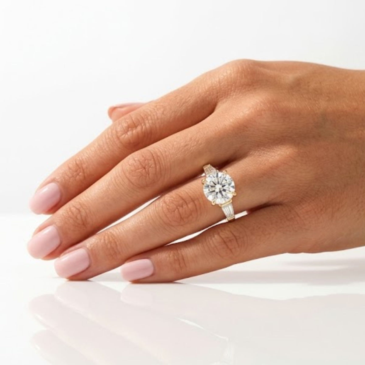 Round brilliant cut diamond engagement ring set in yellow gold, flanked by tapered baguette side stones and worn on a hand.
