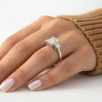 Three-stone radiant cut diamond engagement ring set in white gold or platinum with trapezoid side stones and a polished plain band, worn on a hand.