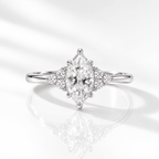 White gold marquise diamond engagement ring with side clusters of three round accent stones each, photographed front-on against a bright white background with a soft reflection.