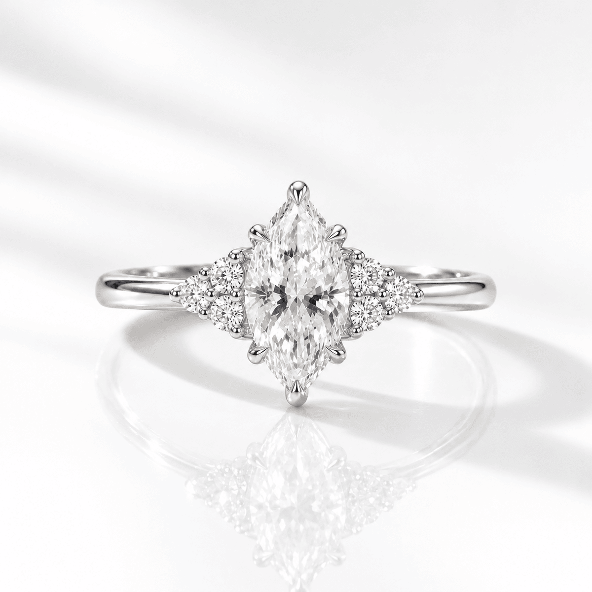 White gold marquise diamond engagement ring with side clusters of three round accent stones each, photographed front-on against a bright white background with a soft reflection.