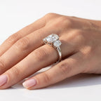 Underside view of a three-stone oval cut diamond engagement ring in white gold or platinum, showing the intricate curved trellis wire basket setting and plain band.