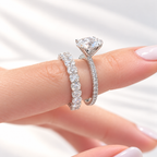 Fingers with a French manicure holding a white gold oval diamond engagement ring with a pavé shank and a matching wedding band of oval diamonds