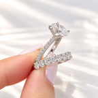 Fingers with a French manicure holding a white gold oval diamond engagement ring with a pavé shank and a matching wedding band of oval diamonds