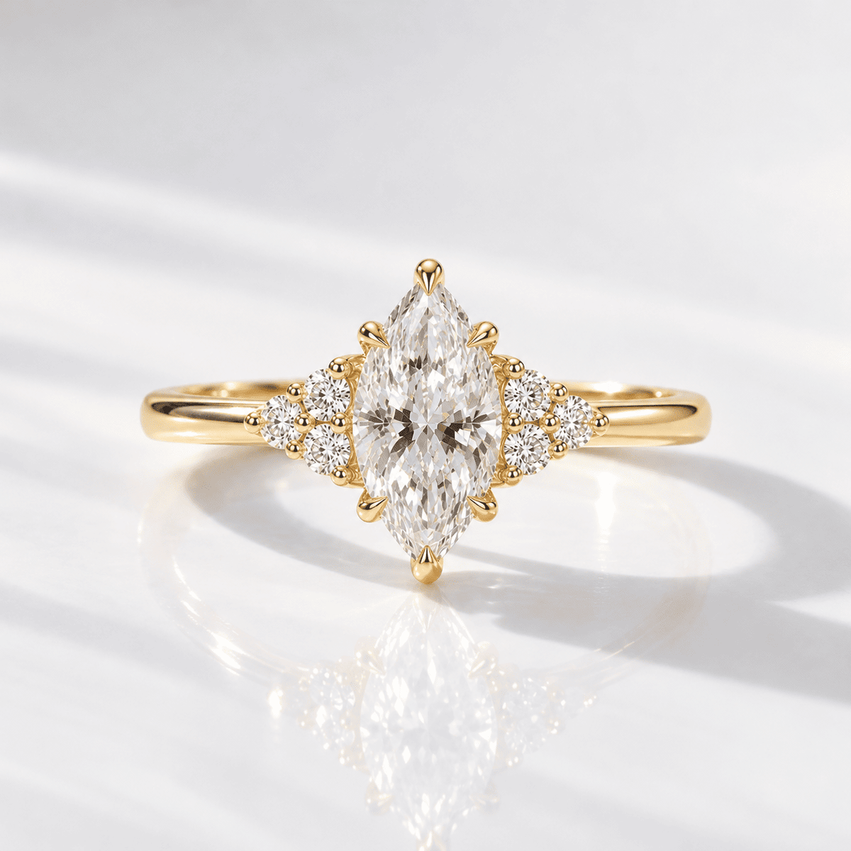 Yellow gold engagement ring with a marquise-cut center diamond, six prongs, and a trio of small round diamonds on each side, shown on a glossy white surface with soft shadows.