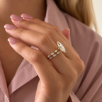 Side view of a hand with pink nails wearing a yellow gold marquise diamond engagement ring stacked with a wedding band of bezel-set marquise diamonds, in front of a pink shirt