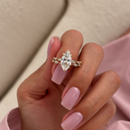 Hand with soft pink nails holding up a finger wearing a yellow gold marquise diamond engagement ring stacked with a bezel-set marquise and round diamond wedding band