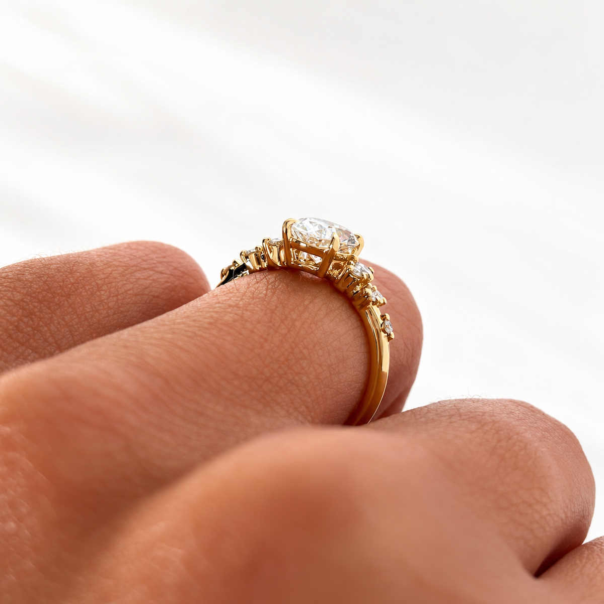 Angled side view of a yellow gold oval diamond ring on a finger, showing the four-prong setting and scattered round diamond accents on the band