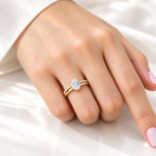 Hand with a light pink manicure wearing a yellow gold oval diamond solitaire engagement ring stacked with a slim pavé diamond wedding band, resting on white satin fabric