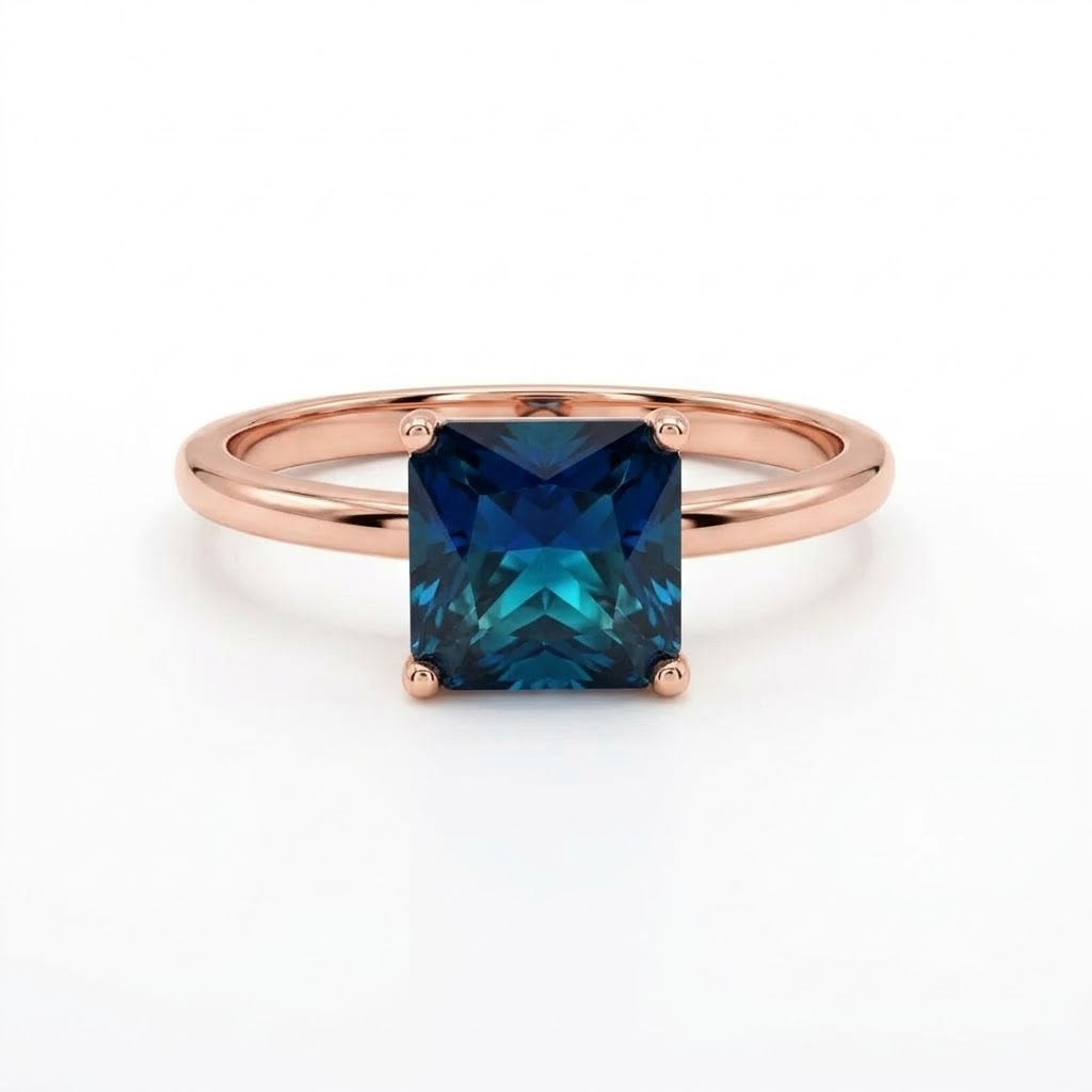 A rose gold ring featuring a square-cut, brilliant-cut deep blue gemstone, shown on a clean white background.