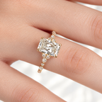 Hand wearing a yellow gold radiant cut diamond engagement ring with trio diamond clusters and a band of round diamonds