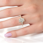 Hand with a lilac manicure wearing a yellow gold radiant cut diamond engagement ring with small diamond clusters beside the center stone